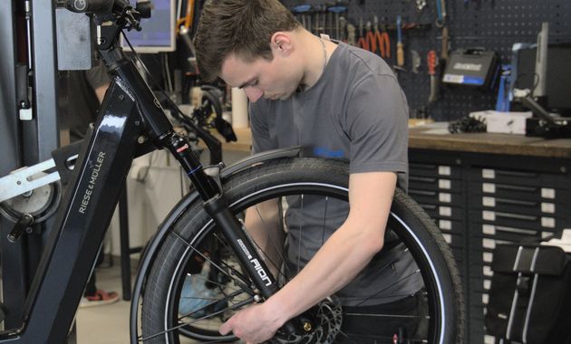 Mechaniker prueft in der Werkstatt das Vorderrad eines Fahrrads